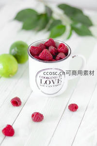印有'烹饪即爱'字样的搪瓷杯盛满覆盆子，青柠点缀白木桌
