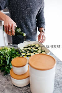厨师正在为切片西葫芦淋橄榄油，准备健康烘焙料理，背景为厨房收纳罐