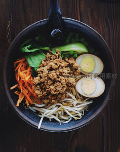 黑陶碗盛肉末蔬菜拉面，配溏心蛋与豆芽，木质背景俯拍
