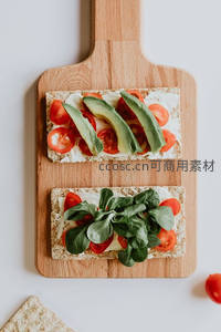 木质砧板上两片全麦吐司开放式三明治，饰以牛油果番茄与芝麻菜