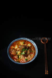 俯拍视角下的红烧牛肉面，配木质筷架，黑背景凸显浓郁风味