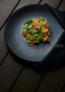 黑釉纹理盘中精致三文鱼沙拉，绿叶胡萝卜丝点缀，木质桌面静谧呈现