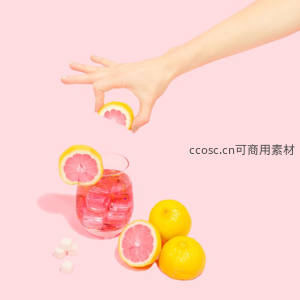 粉背景下手持西柚片投入冰镇粉红饮，糖块与完整西柚环绕，色彩明快时尚
