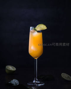 橙色气泡果汁高脚杯特写，青柠叶与冰块点缀深色背景