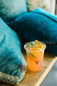 橙色莫吉托塑料杯置于木质托盘，蓝绿靠垫营造居家惬意氛围