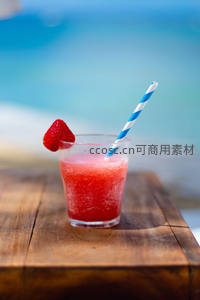 海边木桌上草莓冰沙特写，蓝白条纹吸管与鲜果装饰