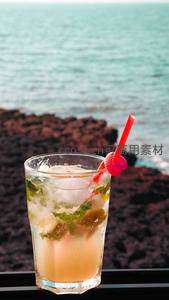 海边岩石旁的薄荷莫吉托鸡尾酒特写，红吸管点缀清新夏日氛围