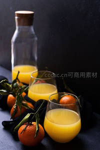深色背景下鲜榨橙汁与带叶柑橘静物组合，玻璃瓶与杯具呈现质感对比