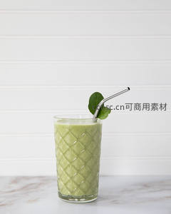 菱格纹玻璃杯中的绿色蔬果昔，配金属吸管与羽衣甘蓝叶，简约白墙背景