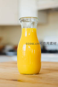 玻璃壶装鲜榨橙汁置于木质台面，背景厨房虚化清新自然