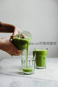 双手倾倒羽衣甘蓝绿汁入玻璃杯，大理石台面清新自然