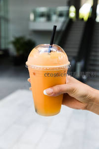 手握泰式奶茶冰饮，橙色奶盖与珍珠清晰可见，都市街头休闲时刻