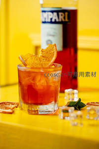 经典内格罗尼鸡尾酒特写，金巴利酒瓶为背景，橙皮卷与薄荷点缀亮黄桌面