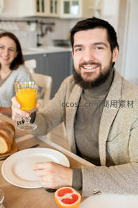 微笑男士手持橙汁杯，厨房背景中享受温馨家庭早餐时光