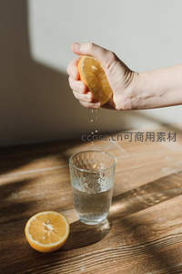 手挤橙汁入杯瞬间，水珠飞溅，木质桌面光影清新自然