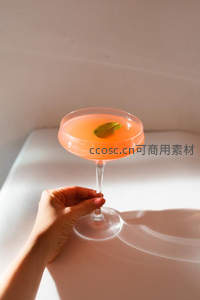 手握橙色鸡尾酒杯，光影交错下的精致瞬间