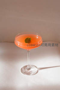 单杯橙色鸡尾酒静置桌面，薄荷点缀光影流动