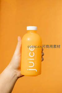 手持冷压橙汁瓶特写，纯橙色背景突出简约健康理念