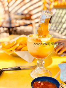 户外市集黄色桌面上，啤酒瓶倒插于盐边玛格丽特杯中，配薯片与莎莎酱