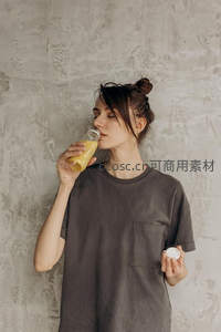 年轻女子闭眼啜饮鲜榨橙汁，灰色工业风背景简约自然