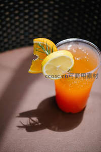 柠檬橙片与迷迭香点缀橙色气泡饮，阳光投射清晰阴影于皮革桌面