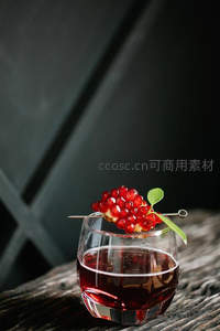 深色背景下的石榴籽装饰红酒杯特写，木质桌面衬托高级感