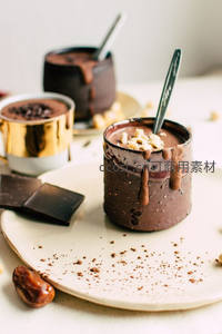 粗陶杯盛巧克力慕斯，可可粉洒落盘面，配金杯与黑巧块