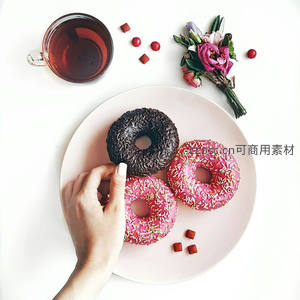 手取巧克力与草莓糖霜甜甜圈，搭配红茶与花束的极简俯拍