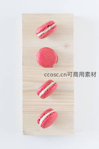 四枚粉红马卡龙垂直排列于浅木板上，奶油夹心清晰可见