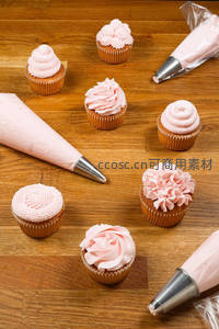 木质桌面上多款粉色奶油裱花纸杯蛋糕与裱花袋组合