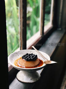 窗边焦糖布丁配黑珍珠，粗陶器皿盛装，绿植光影映衬静谧午后