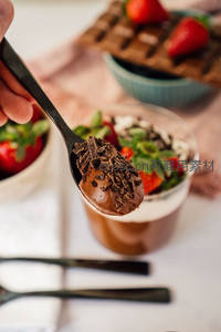 黑勺盛巧克力慕斯配碎巧与草莓，背景甜点朦胧温馨