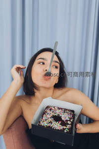俏皮女子用叉子平衡巧克力蛋糕，背景蓝帘温馨惬意
