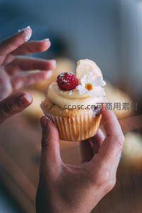 手捧精致纸杯蛋糕，覆奶油、覆盆子与雏菊的温柔特写