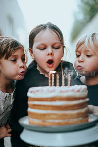 三个孩子合力吹灭生日蛋糕蜡烛，温馨自然光下的童年瞬间