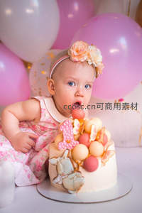 可爱女婴戴花环吹生日蛋糕，粉色气球环绕温馨庆祝