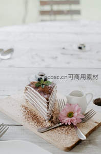 千层蛋糕切片摆于木板，撒可可粉配薄荷叶与粉色雏菊，清新雅致