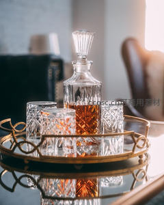 水晶醒酒器与雕花玻璃杯置于镀金托盘，琥珀色烈酒折射暖光