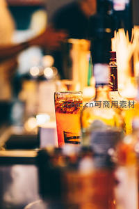 酒吧吧台特写：冰块摇曳的鸡尾酒杯与模糊酒瓶构成温暖光晕