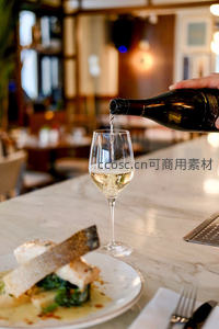 餐厅吧台白葡萄酒斟入杯中，配烤鱼主菜，环境温馨雅致