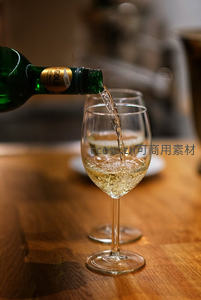 白葡萄酒倾倒入高脚杯，木质桌面光影流动瞬间