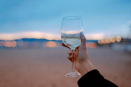 黄昏沙滩举杯白葡萄酒，城市灯火虚化成梦幻光斑
