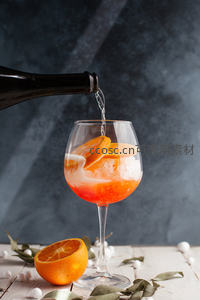橙片装饰的气泡酒倾倒瞬间，冰块与琥珀色液体交融