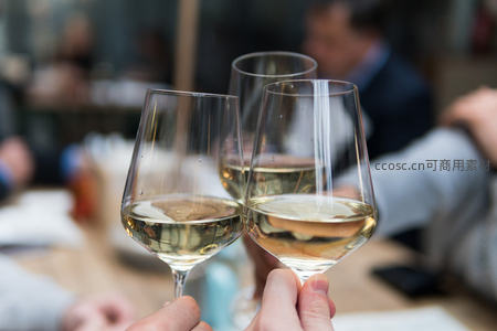 三只高脚杯盛白葡萄酒轻碰，背景人群模糊，展现优雅品酒社交瞬间