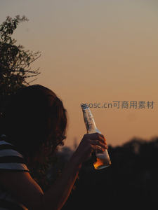 剪影女子手持啤酒瓶仰望夕阳，暖色调天际线勾勒宁静独酌时光