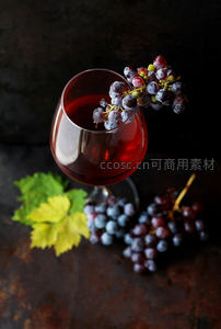 深红葡萄酒杯旁缀紫葡萄串，绿叶点缀，暗调背景凸显醇香质感