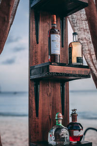 海边木架陈设威士忌与龙舌兰，海天暮色为背景，展现度假微醺情调