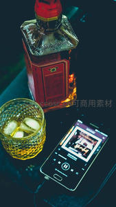 方瓶威士忌、冰镇酒杯与播放音乐的智能手机构成现代夜生活场景