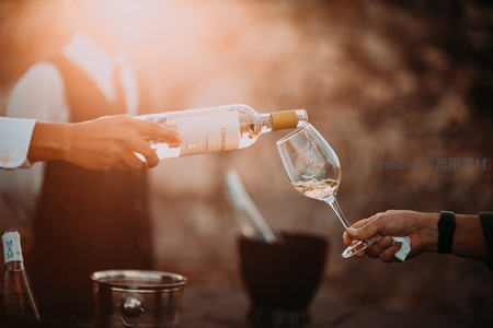 侍酒师倾倒白葡萄酒，金色光晕中液体优雅入杯