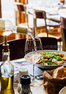 餐厅中白葡萄酒倾倒入杯瞬间，搭配沙拉与面包的惬意用餐场景
